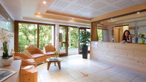 Un área de recepción moderna con mobiliario de madera, un mostrador de recepción y grandes puertas de cristal que dan a un jardín.