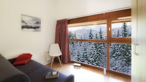 Un salón moderno con un sofá, un sillón y un amplio ventanal con vistas a una montaña nevada.
