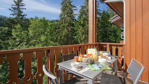 Un balcón con una mesa lista para el desayuno, rodeado de barandas de madera, con vista a una zona boscosa.