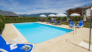 A rectangular swimming pool with clear blue water, surrounded by blue lounge chairs and umbrellas.