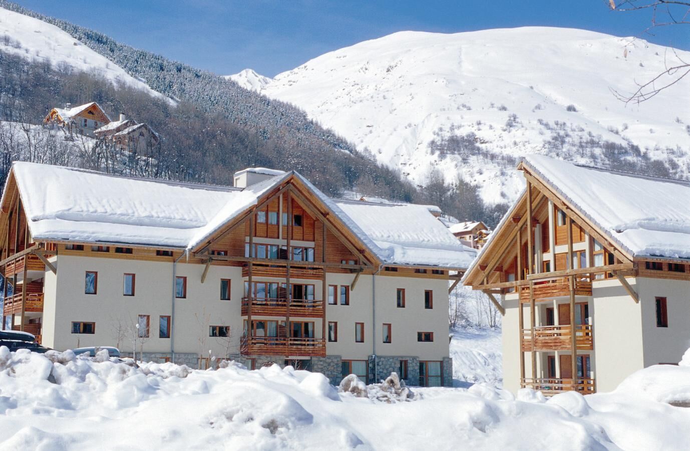 Un edificio de estilo chalet con fachada de madera y varios balcones, rodeado de montañas nevadas.