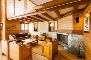 Interior acolhedor de uma cabana de madeira com lareira de pedra, móveis de madeira e uma televisão.
