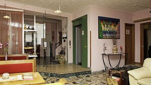 Eine Hotelhalle mit Glastrennwand, einem grünen Aufzug, einem Gemälde an der Wand und einem Tisch mit Vase und Kerzen.