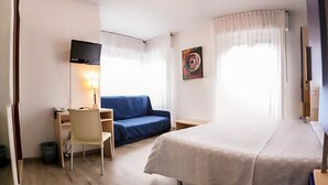 Ein Hotelzimmer mit einem Bett, einem Schreibtisch mit Stuhl, einer Couch, einem Fernseher und einem Bild an der Wand.