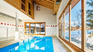 Une piscine intérieure avec des poutres en bois, de grandes fenêtres et une vue sur un paysage enneigé.