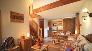 Un salon chaleureux avec un escalier en bois, un coin repas et une cuisine.