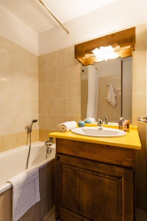 A bathroom with a bathtub, a sink with a mirror above it, and wooden cabinets.