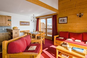 A cozy log cabin interior with a dining area, a sofa, and a table with a book and a bottle. - 200m from resort center, swimming pool, sauna, hammam, terrace, balcony, tv, ski locker, 50m² (Fontcouverte-la-Toussuire)
