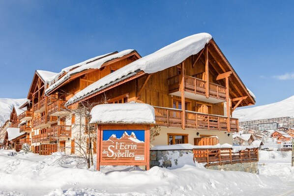A wooden chalet with balconies, surrounded by snow, labeled "Alpin des Sybbels."