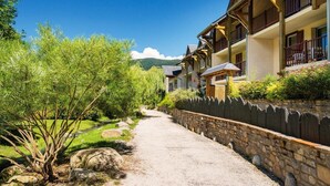 A row of traditional wooden buildings with balconies, a gravel path, and surrounding greenery. - Swimming pool, sauna, hammam, terrace, balcony, parking, tv, ski locker, 48m², Saint Lary Soulan (Saint-Lary-Soulan)