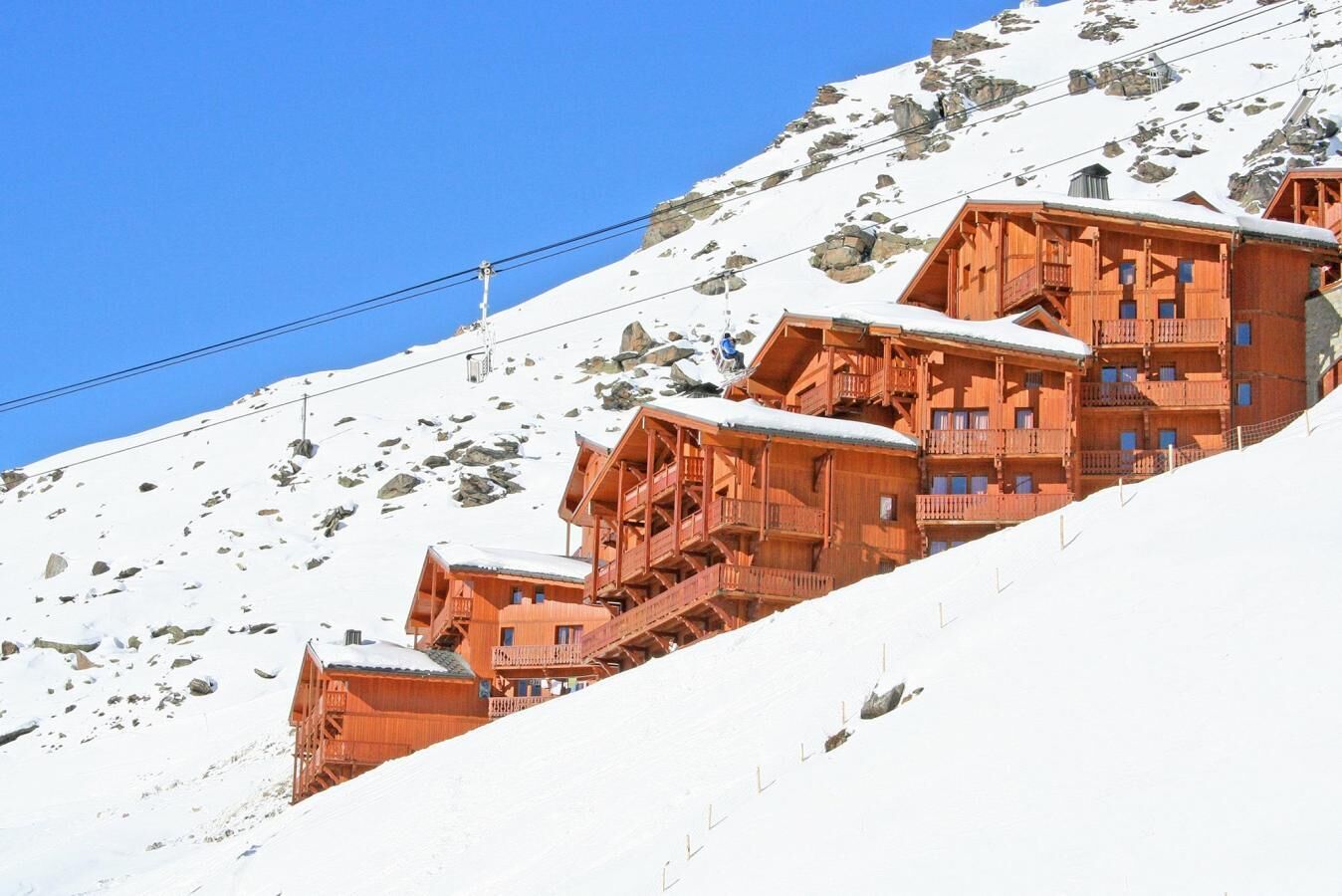 Een houten hotel in chaletstijl met meerdere balkons en een besneeuwde berg op de achtergrond.