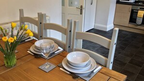 A dining table set with white plates, bowls, and cutlery, accompanied by a glass of water and a vase of yellow flowers. - Shaw Properties Teal Road (Darlington)