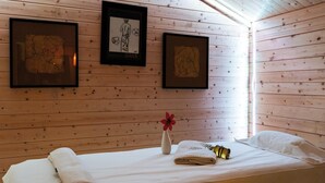 Una habitación de cabaña de madera con una cama, toallas, un florero con una flor y cuadros en la pared.