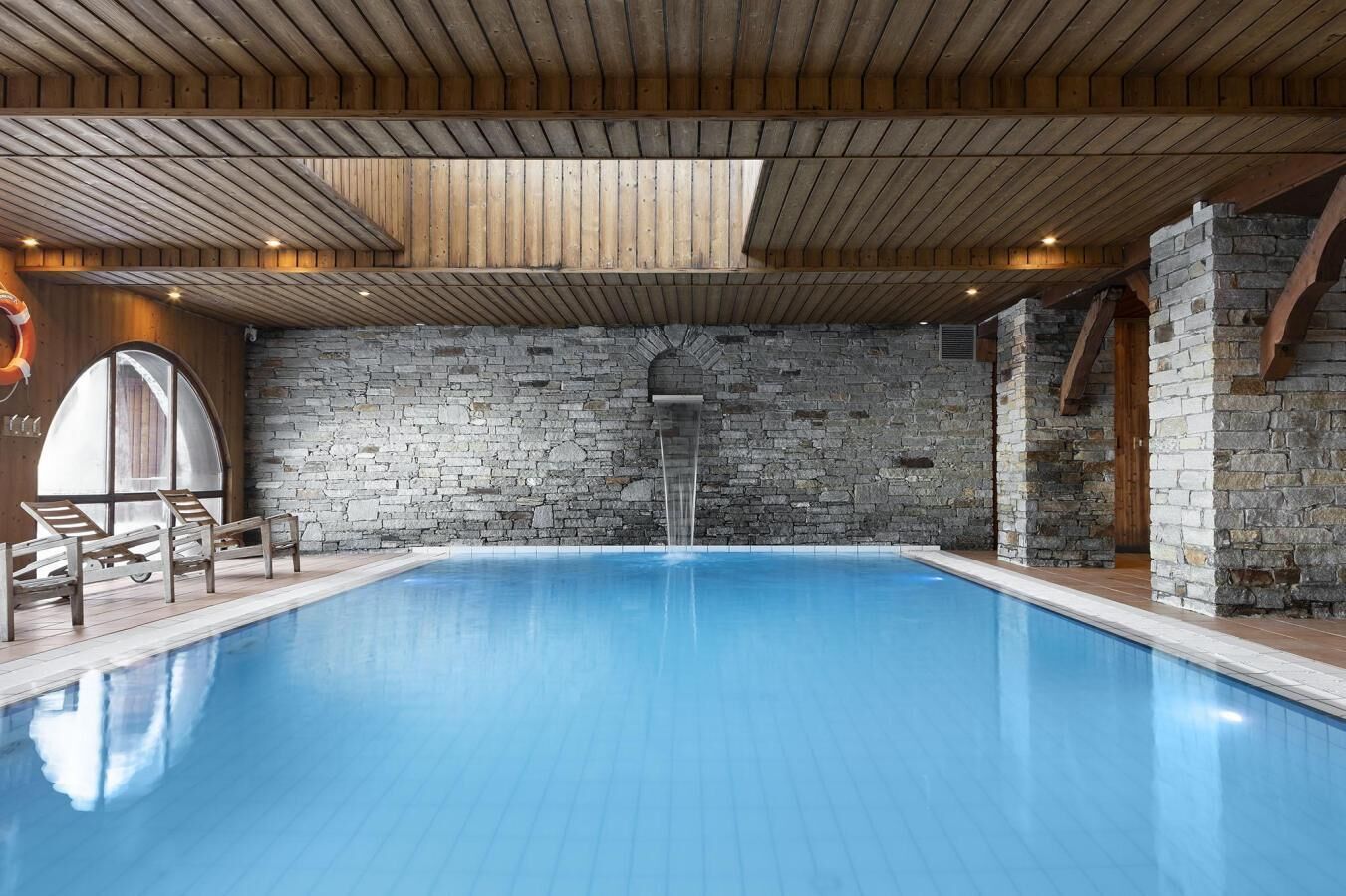 Una piscina interior con paredes de piedra y vigas de madera en el techo.