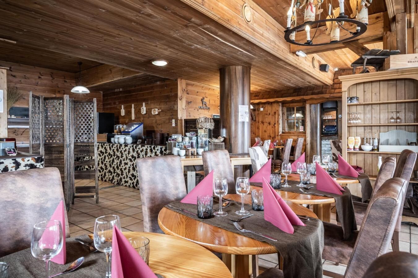 Un restaurant au décor intérieur en bois, avec des tables nappées de serviettes roses et des verres à vin.
