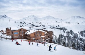 Ein Skigebiet mit Holzhäusern, Skipisten und schneebedeckten Bergen.