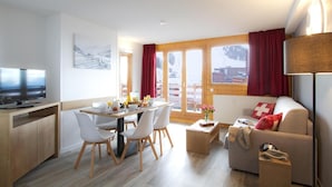 Un salon moderne comprenant un coin repas, un plancher en bois, un canapé avec des coussins rouges, un téléviseur et une fenêtre avec des rideaux.