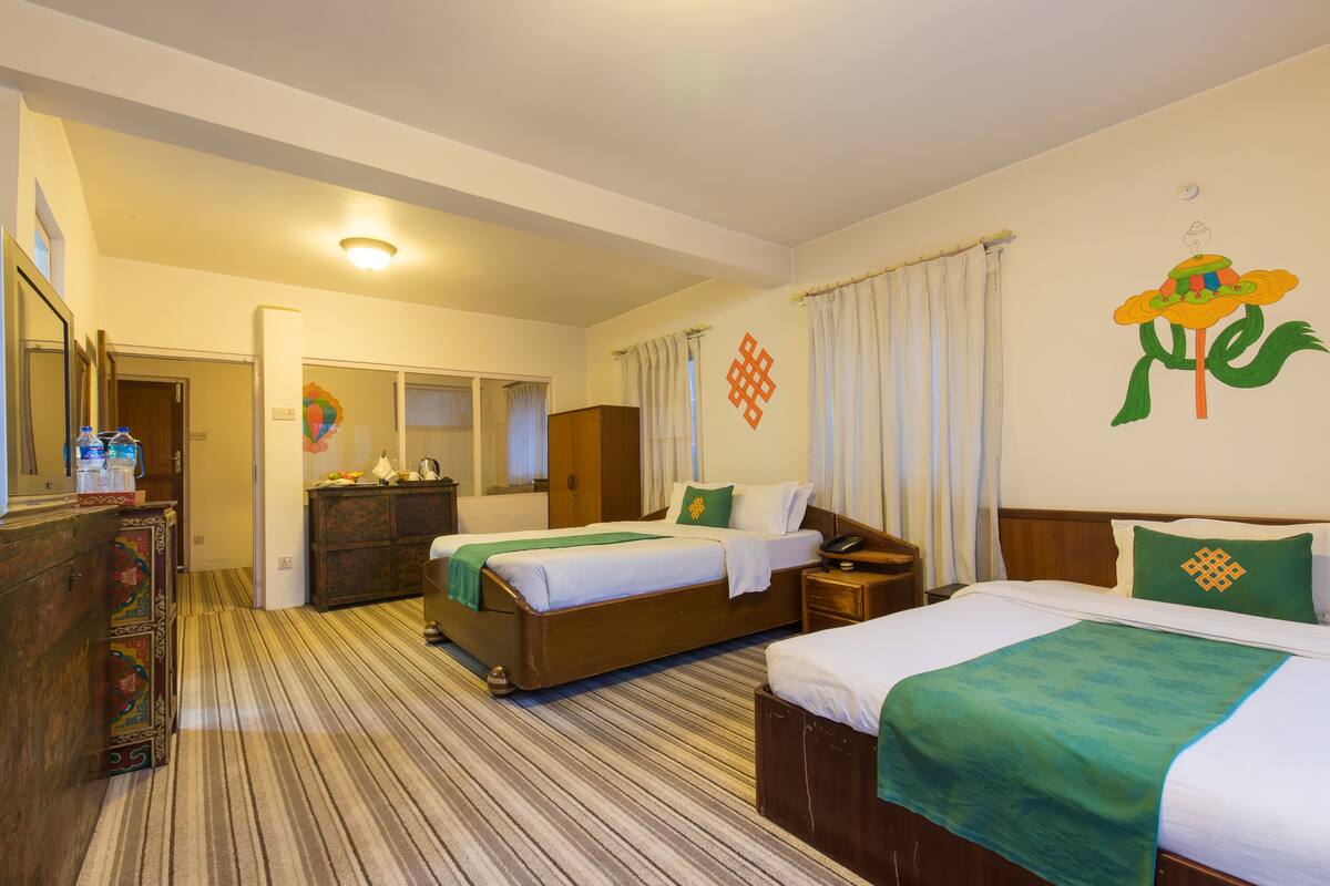 Une chambre d’hôtel avec deux lits, une commode en bois, un miroir et un mur orné d’un motif floral.