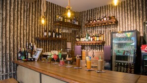 Una zona de bar con estantes de madera que sostienen botellas y vasos, un mini bar y un refrigerador expositor.