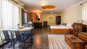 Habitación de hotel con comedor, kitchenette y cama con cabecera de madera.