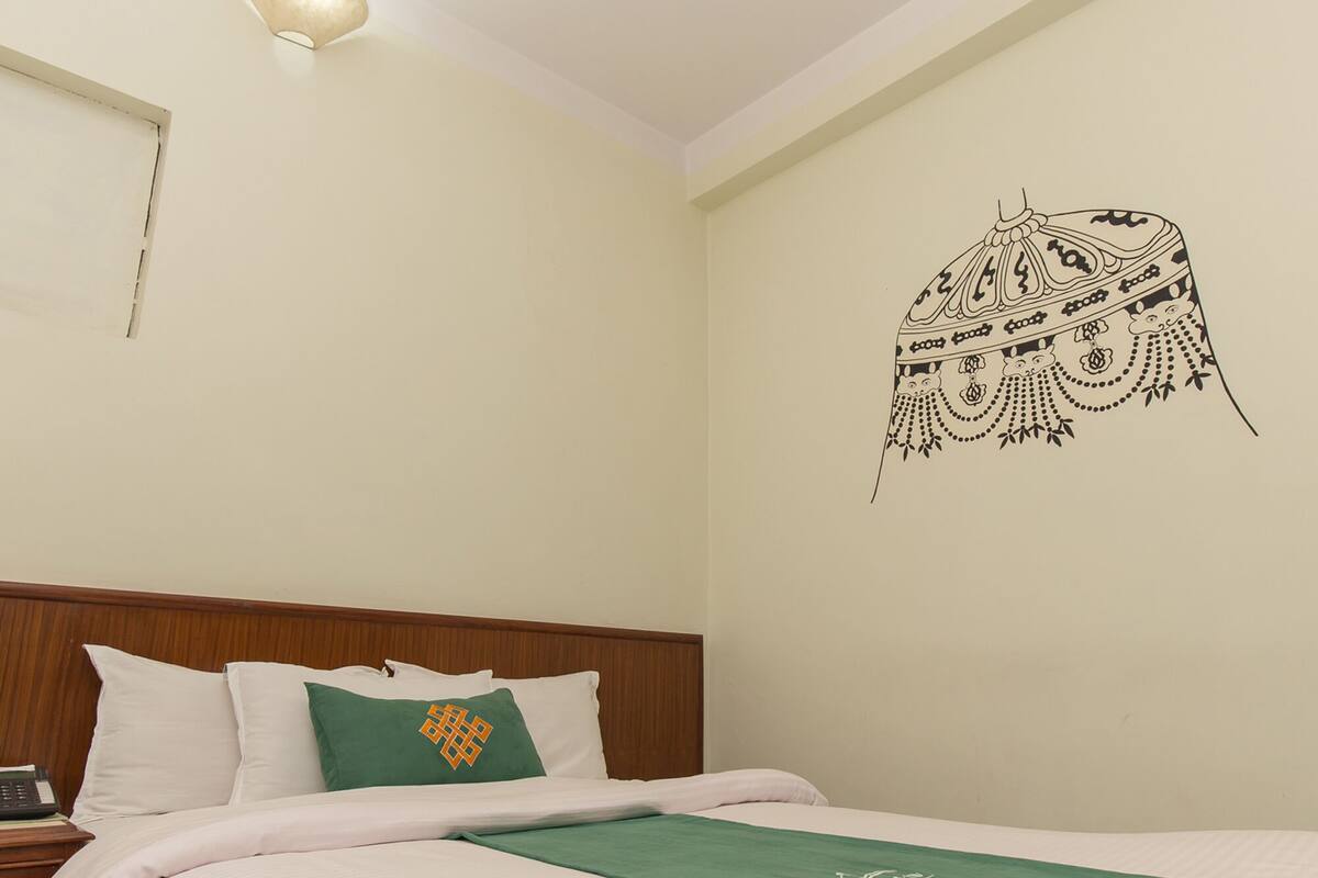 Une chambre d’hôtel avec un lit bien fait, une table de chevet avec une lampe et un élément décoratif au mur.