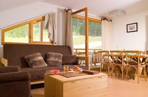 A cozy living room with a brown sofa, a wooden coffee table, and a dining area with wooden chairs.