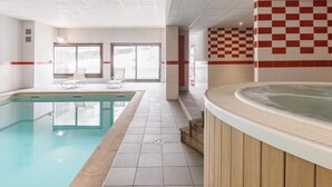 Una piscina interior con jacuzzi, paredes enlosadas y vistas al exterior.