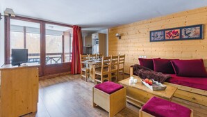 Interior acogedor de una cabaña con una zona de comedor de madera, un sofá con cojines rojos y un televisor sobre un mueble de madera.