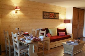 Ein Holzinnenraum mit einem Esstisch für vier Personen, einem roten Sofa mit Kissen und einem kleinen Holzschrank.