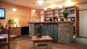 Una habitación acogedora con detalles de madera, una chimenea de piedra, una mesa de madera con un florero, y una zona de bar con estantes llenos de botellas y vasos.