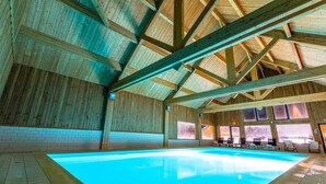 Une piscine intérieure avec des poutres en bois et de grandes fenêtres.
