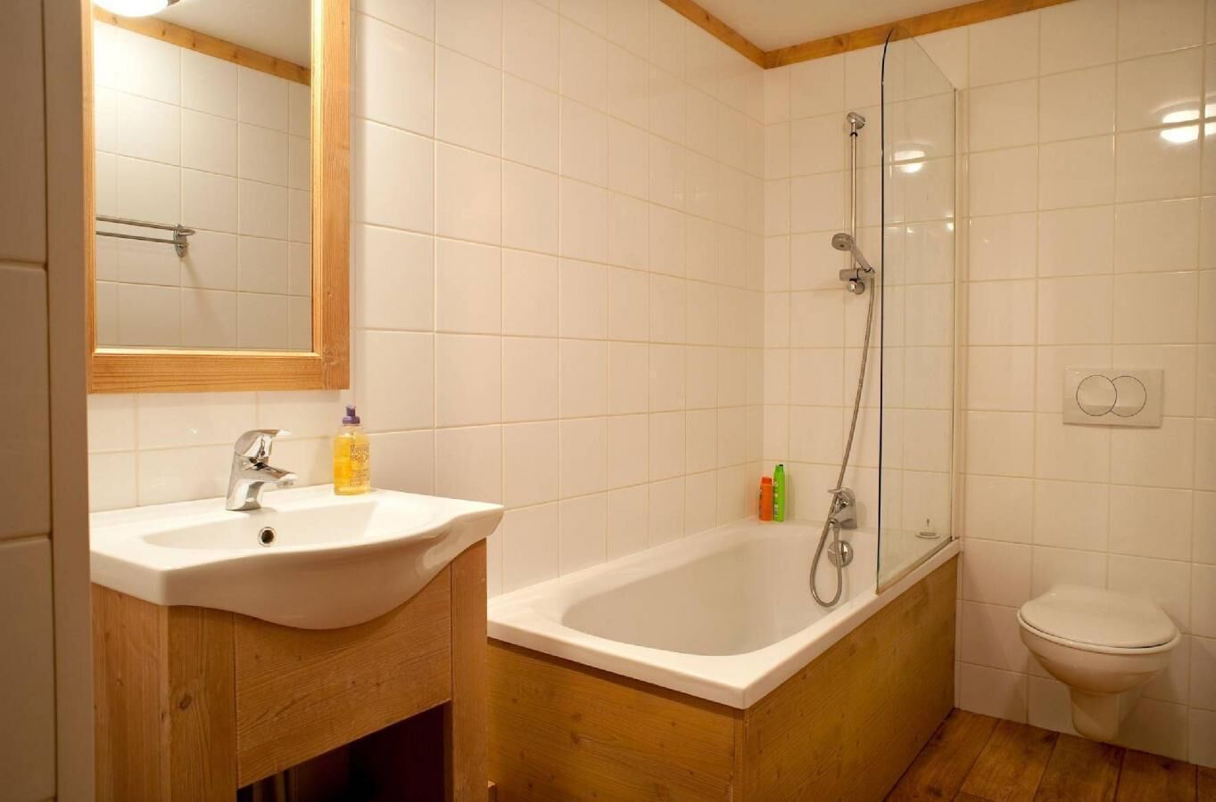 A bathroom with a white sink, wooden cabinet, glass shower enclosure, and a toilet.