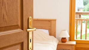 A wooden door with a brass handle, a bed with white bedding, a nightstand with a lamp, and a view of a balcony. - Wifi, Ground floor, swimming pool, sauna, terrace, balcony, parking, ski locker, 35-42m², La Féclaz (La Féclaz)