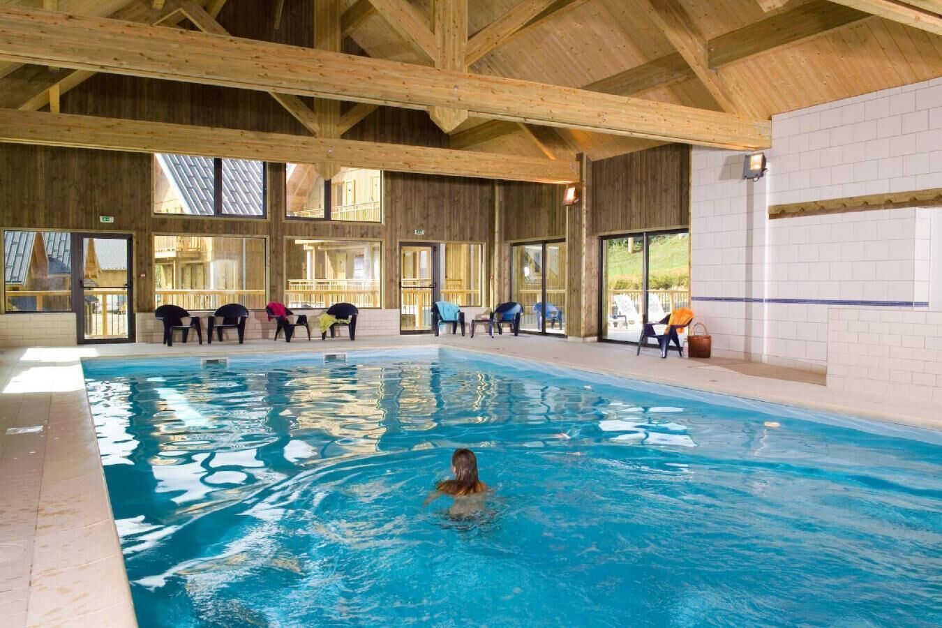 An indoor swimming pool with wooden beams, clear glass windows, and lounge chairs.