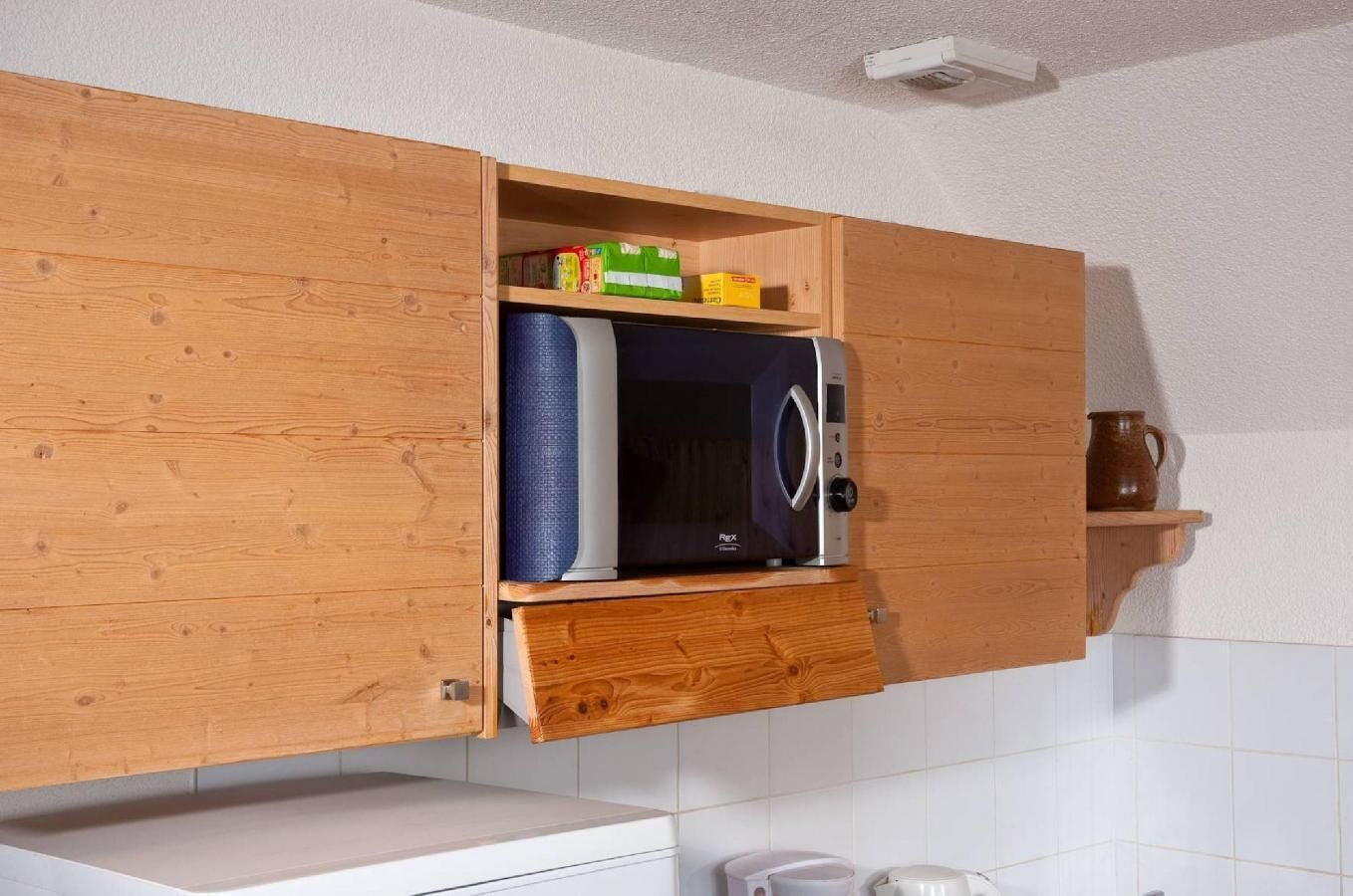 A kitchen with wooden cabinets, a microwave, and a small shelf with a jug.
