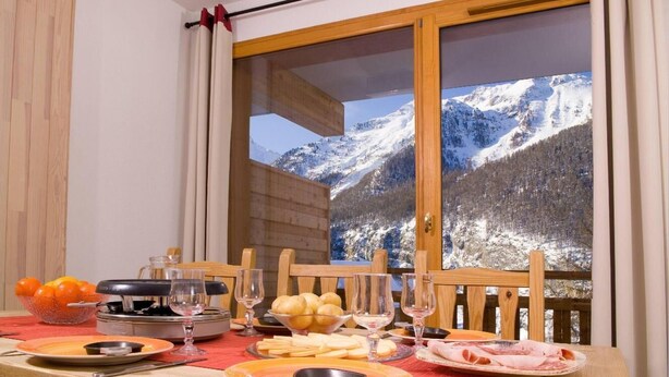 A dining table set with plates, glasses, and food items, with a mountain view through a window. - 50m from shops, swimming pool, balcony, 36-37m², Les Orres (Les Orres)