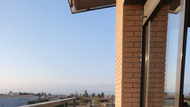 Ein Balkon mit Tisch und zwei Stühlen, Blick auf ein Gewässer und eine Ziegelmauer.