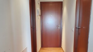 Ein Flur mit Holzboden, einer Tür am Ende und einem Lichtschalter an der Wand.