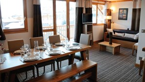 A dining area with a wooden table set for four, a sofa, and a TV in the background.