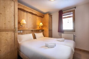 A double room with wooden paneling, two beds, bedside lamps, a window with curtains, and a radiator. - Wifi, ski-in/ski-out & foot of the slopes, swimming pool, sauna, hammam, balcony, tv, ski locker (La Rosière Montvalezan)