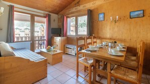 A wooden interior with a dining table set for four, a sofa, and a television on a cabinet.