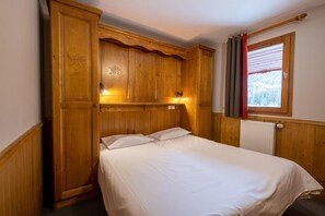 Habitación de madera con cama, armario y ventana con cortinas.