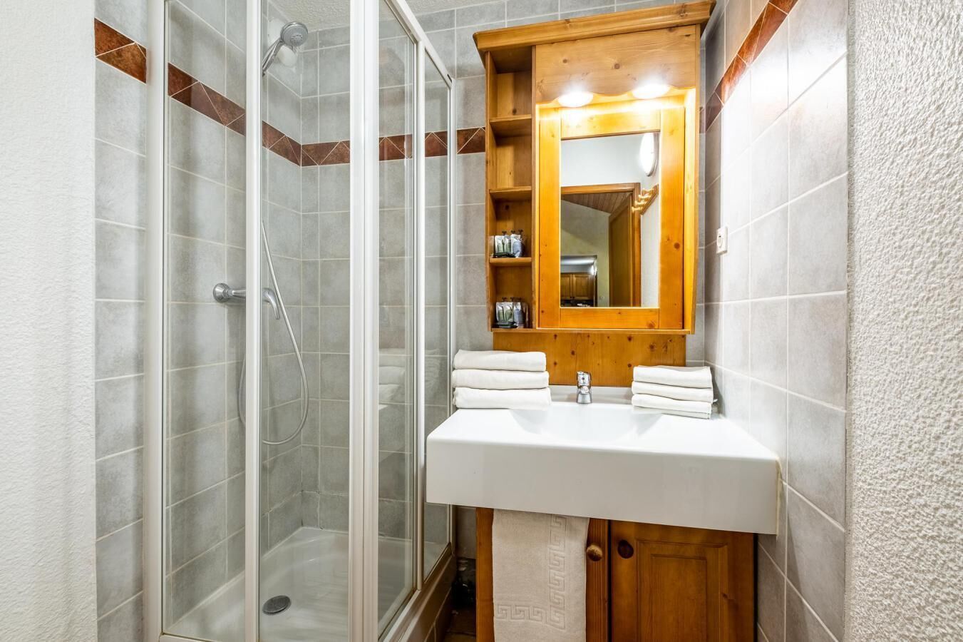 A bathroom with a glass shower enclosure, a wooden vanity with a mirror, and a white sink.