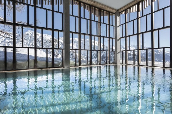 Swim laps in a spacious pool surrounded by a high ceiling and floor-to-ceiling windows offering breathtaking mountain views.