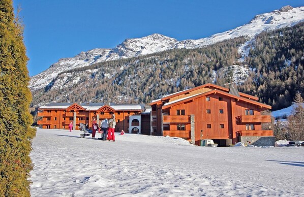Une station de ski avec des bâtiments en bois, un paysage enneigé et des montagnes en arrière-plan.