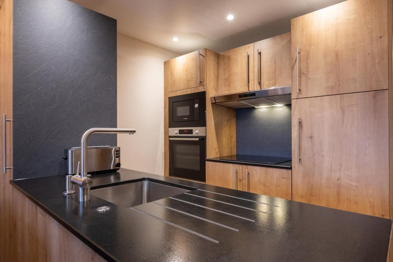 Una cocina moderna con encimera negra, electrodomésticos de acero inoxidable y armarios de madera.