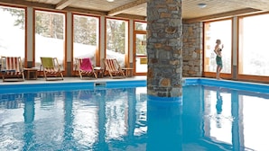 An indoor swimming pool with stone pillars, wooden ceiling, and large windows. - 300m from ski slopes, swimming pool, sauna, hammam, terrace, balcony, tv, ski locker, 37m² (La Plagne)