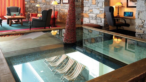 A pool area with lounge chairs, a stone wall, and a wooden deck. - 300m from ski slopes, swimming pool, sauna, hammam, terrace, balcony, tv, ski locker, 37m² (La Plagne)