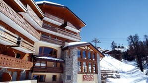 A multi-story hotel with wooden balconies and a stone facade, located in a snowy mountainous area. - 300m from ski slopes, swimming pool, sauna, hammam, terrace, balcony, tv, ski locker, 37m² (La Plagne)