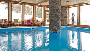 En indendørs swimmingpool med stensøjler, træloft og store vinduer.